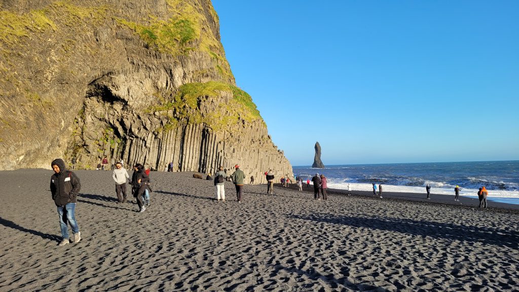 tourists on a black sand beach with basalt rock formations