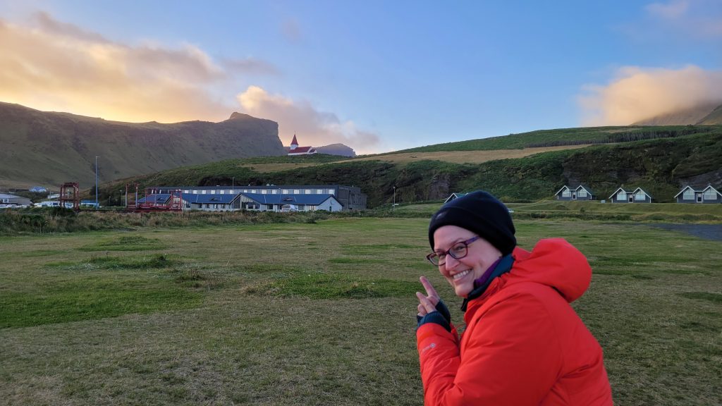 Susan pointing at Vík's church on a hilltop near the campground