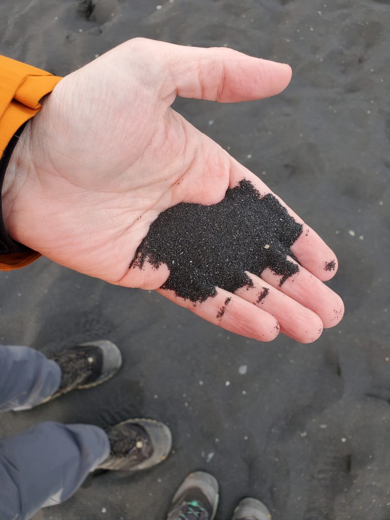 black sand in Graham's hand with our feet down below on the black sand beach