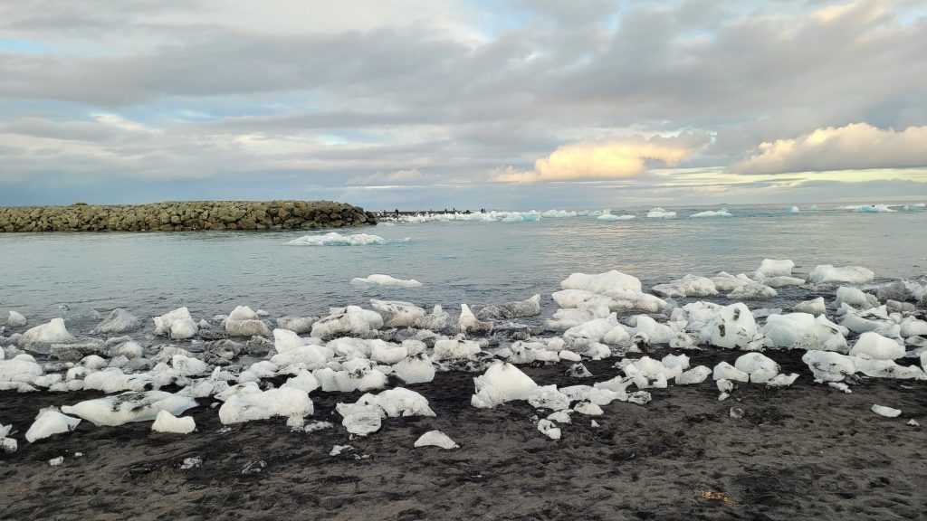 ice chunks on a black sand beach with the ocean behind them.