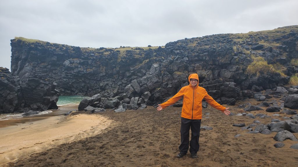 man in orange rain jacket standing on the beach